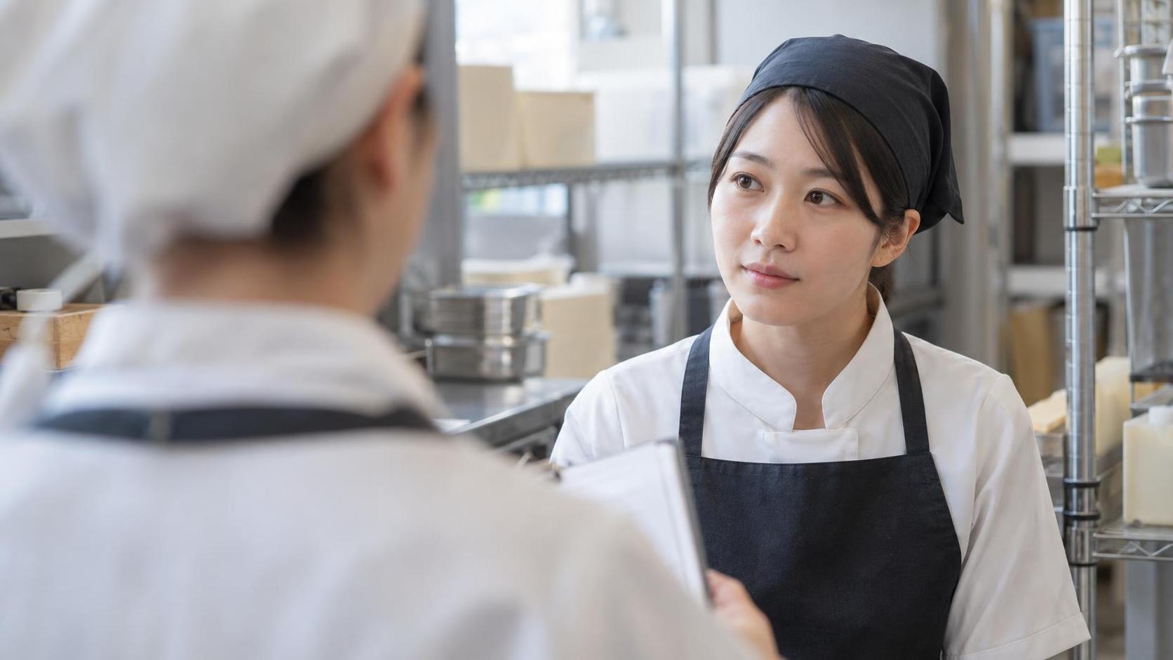 バックヤードで短い打ち合わせをする制服のスタッフ2人