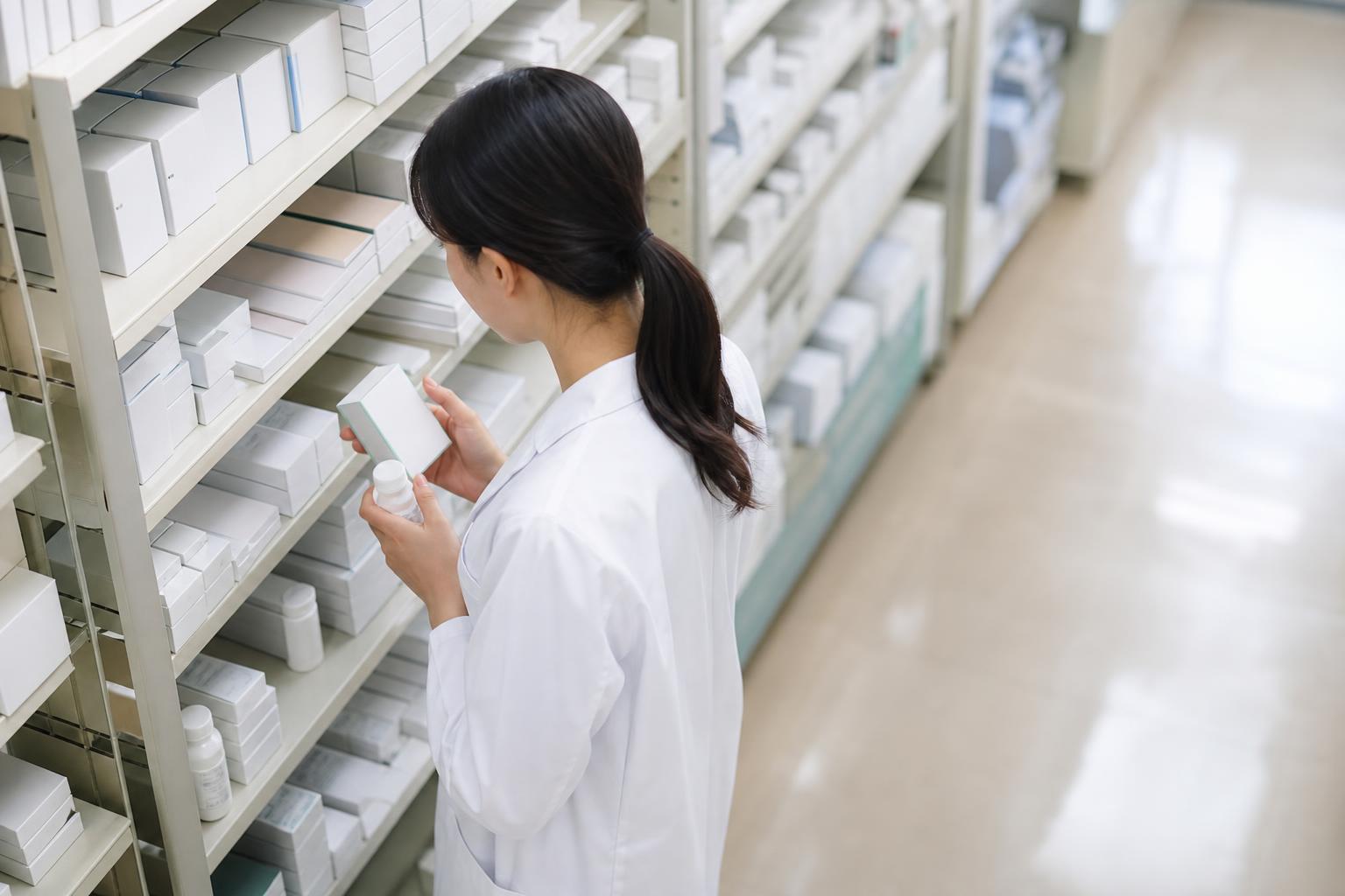 棚の前で在庫を確認する白衣の薬剤師